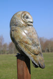 Bronze sculpture of an owl on a tall pole in a garden setting