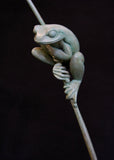 Bronze sculpture of a tree frog on a branch against a black background