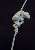 Bronze sculpture of a tree frog on a branch against a black background