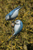 Bronze sculpture of two blue birds perched on a branch with a blurred green background