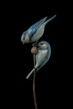 Bronze sculpture of two blue birds on a branch with a black background