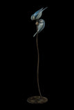 Bronze sculpture of two blue birds on a branch with a black background