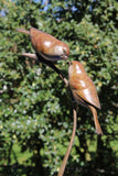 Bronze sculpture of two birds perched on a branch against a green leafy background