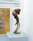 Bronze sculpture of an otter on a glass platform with a painting in the background