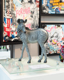 Zebra bronze sculpture on a glass table with colourful artwork in the background
