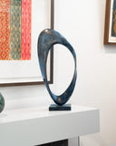 Abstract sculpture on a white surface with framed artwork in the background