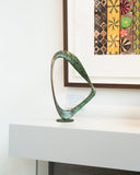 Abstract sculpture on a white surface with a colorful framed artwork in the background