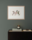 Framed artwork of birds on a gray wall above a console table with a candle and books.