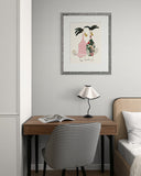Small desk with chair, lamp, and framed artwork on a wall in a room.
