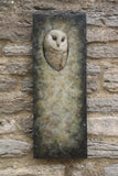 A rectangular stone wall plaque featuring a carved or sculpted barn owl head set into a textured, weathered stone background, mounted on a rustic stone wall.