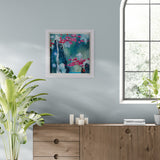 Framed abstract painting on a wall above a wooden cabinet with plants around.