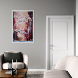 Framed abstract painting on a gray wall above a chair with a wooden table and books.