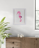 Framed pink seahorse artwork on a wall above a wooden cabinet with candles.