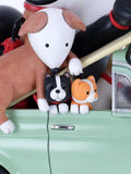 A close-up of a decorative figurine or toy scene showing three small dog-like characters sitting on the edge of a mint green vehicle. The largest figure is white and tan, with two smaller figures in black-and-white and orange-and-white.