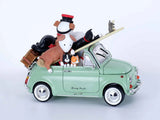 A mint green toy car with cartoon characters and luggage piled into its trunk and roof, photographed on a clean light gray studio background.