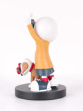 A stylized figurine of a person with a large white head, wearing an orange top, dark skirt, and blue-and-white sneakers, standing on a round black base next to a small brown dog with red and white accessories, photographed on a white background.