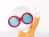 A white spherical character figurine wearing red-rimmed round glasses with light blue lenses and a yellow-orange shirt, holding up a peace sign on a white background.
