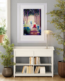 A framed vertical art print depicting a colorful forest path with a red umbrella, displayed on a gray wall above a white console table in a styled room setting.