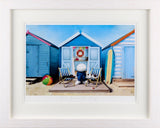 Framed photograph of a beach scene with colorful huts, a teddy bear, and beach accessories.
