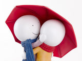 Two white spherical characters hugging under a red umbrella on a white background