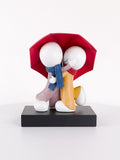 Decorative figurine of two characters under a red umbrella on a white background