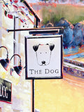 A painted storefront sign for "The Dog" featuring a simple black line drawing of a dog head on a white square panel, mounted on a pole beside two black wall lamps.