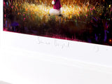 A framed art print featuring an impressionistic painting of a small white and magenta figure in a field of golden grass, with a wide white mat and a handwritten signature near the bottom.