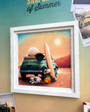 A framed art print featuring a whimsical sunset scene with a teal van, surfboard, dog, and cat, displayed on a teal and beige wall with other photos pinned nearby.