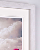 Close-up of a framed art print showing a cloudy sky with pink and purple balloon tops visible at the bottom, featuring a white textured frame and white mat.