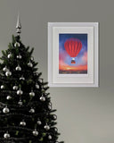Decorated Christmas tree with silver ornaments next to a framed artwork of a hot air balloon.