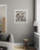 A framed abstract painting of a horse's head in white, gray, and black tones, displayed on a gray wall in a modern living room setting.