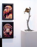 Framed artwork of a monkey on a white wall with a sculpture of a monkey on a branch.