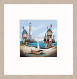 A framed art print featuring a whimsical coastal scene with colorful houses, a lighthouse, blue water, and a small sailboat, presented with a whitewashed oak frame.