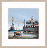 A framed art print featuring a whimsical coastal village scene with a small orange boat on the shore, colorful houses, a lighthouse, and a wooden dock under a pale blue sky.