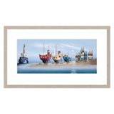 Framed artwork of colorful boats and a lighthouse on a beach.