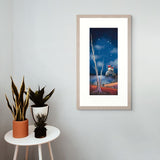 Framed artwork of a starry night scene with a house and tree on a wall above a small table with plants.
