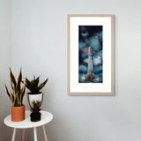 Framed artwork of a lighthouse against a night sky with a small table and plants below.