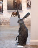 Bronze hare sculpture in an art gallery setting with other artworks in the background.