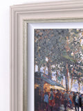 A close-up of a framed painting showing an impressionistic outdoor scene with trees, a building, and a crowd. The frame is a light warm off-white with a subtle metallic inner trim.