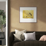 Framed artwork of birds on a yellow background above a brown sofa with gray cushions.