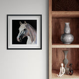 Framed artwork of white horse on a dark background in a black frame on a white wall next to wooden shelves.