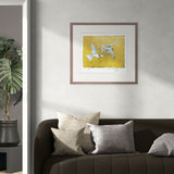Framed artwork of two birds on a yellow background above a sofa with decorative pillows.