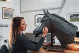 Woman working on a large horse head sculpture in a studio setting.
