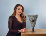 Woman holding a small sculpture of a lion's head on a wooden table with a plain background