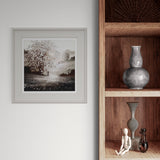 Framed artwork on a wall next to wooden shelves with decorative items