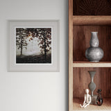 Framed artwork of a forest scene on a wall next to wooden shelves with decorative items.