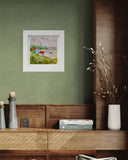 Framed artwork on a green wall above a wooden shelf with decorative items.