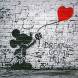 Graffiti of a silhouette holding a rose and a red heart balloon on a brick wall with 'DREAMS COME TRUE' text.