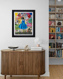 Framed artwork of a girl in a blue dress on a wall above a wooden cabinet with books and decor.