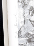 Close-up of a framed artwork with a signature and text on a white background